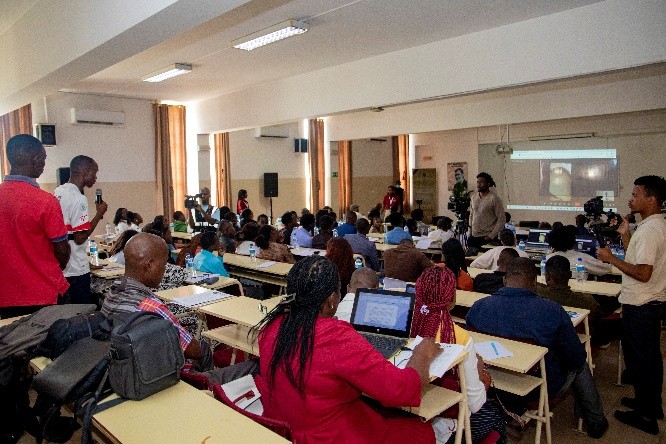Sala de trabalho com participantes acompanhando as apresentações.
